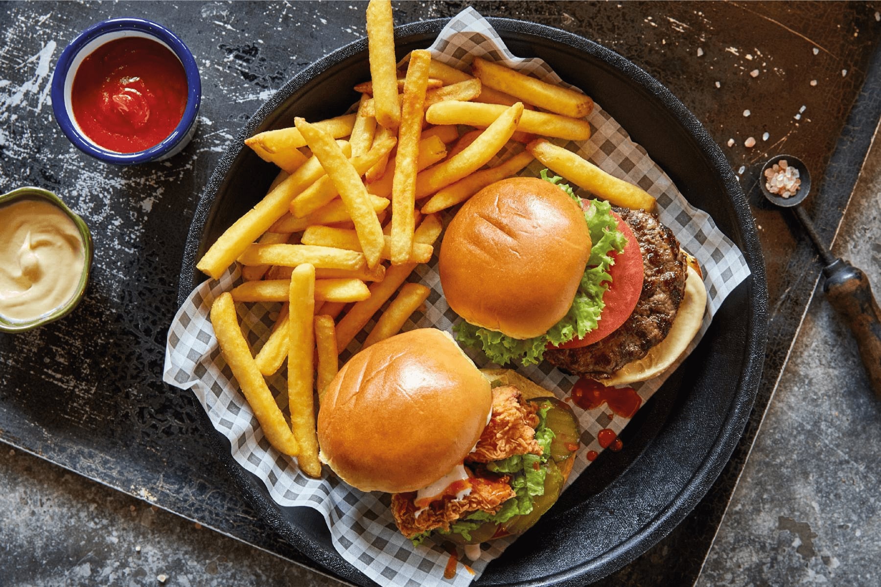 Dwa burgery z frytkami w koszyku, obok sosy