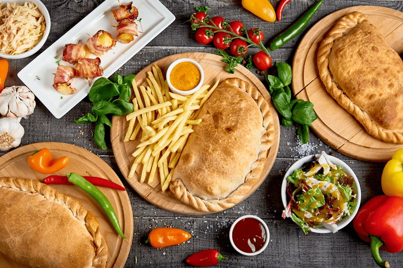 Calzone, frytki i składniki (pomidory, papryka, bazylia) na drewnianym blacie