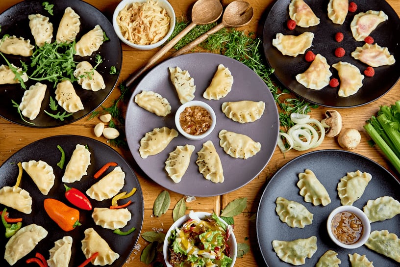 Talerze z pierogami, sosami i warzywami na drewnianym stole