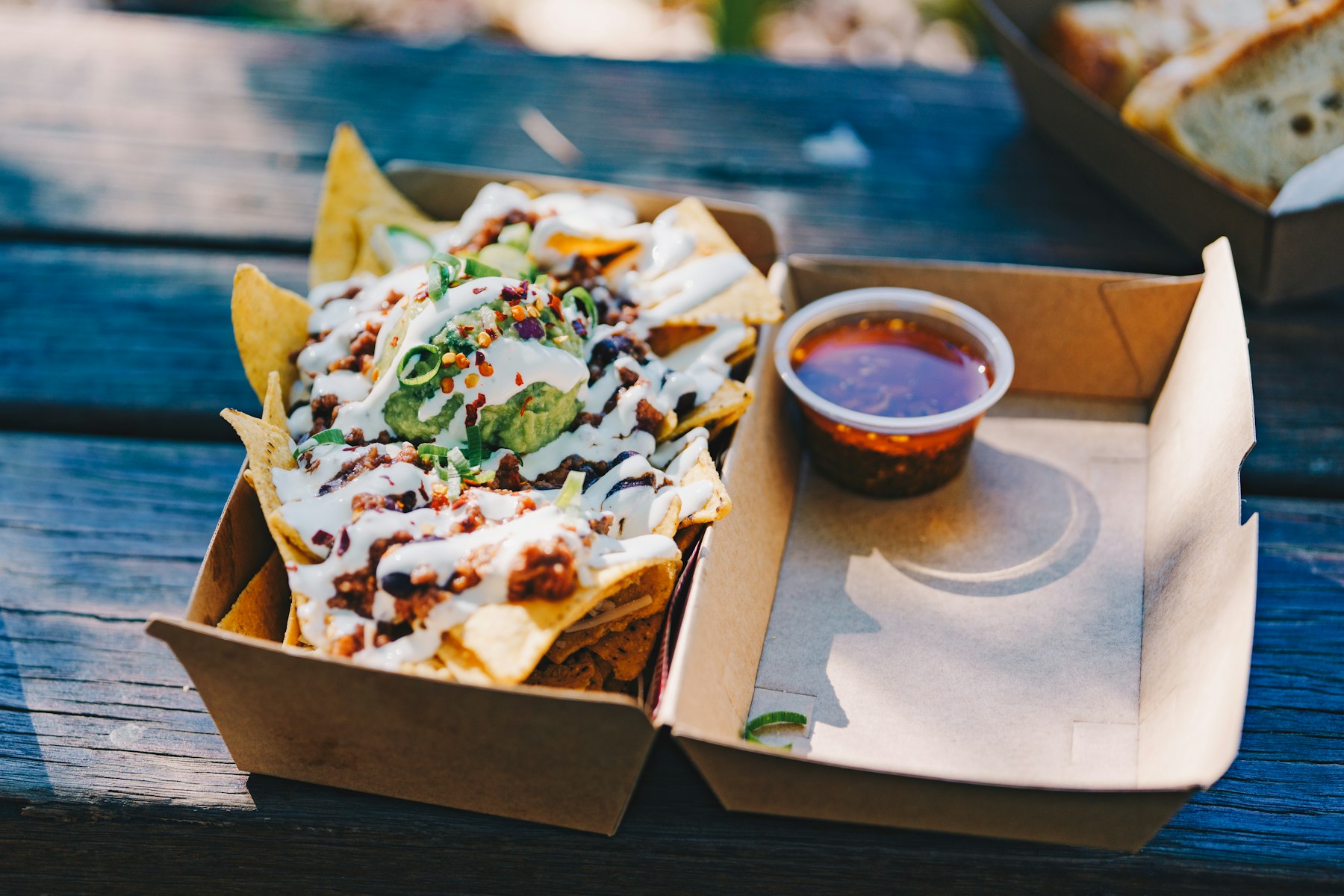 Nachos z sosem w kartonowym pudełku na wynos, obok miseczka z dipem, na drewnianym stole